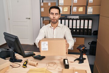 Sticker - Young hispanic man with beard working at small business ecommerce holding box making fish face with mouth and squinting eyes, crazy and comical.