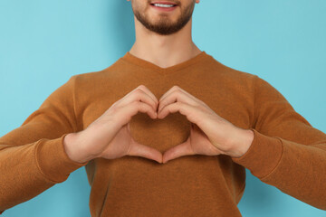 Wall Mural - Happy volunteer making heart with his hands on light blue background, closeup
