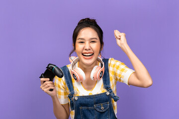 Wall Mural - Beautiful Asian young woman in casual yellow t-shirt and playing video games using joysticks with headphones on voilet background isolated.