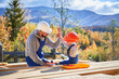 © anatoliy_gleb - Father with toddler son building wooden frame house. Boy helping his daddy, giving high five to kid on construction site, wearing helmet and blue overalls on sunny day. Carpentry and family concept.