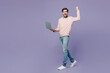 Full body side view young IT man he wearing casual clothes pink sweater glasses hold use work on laptop pc computer do winner gesture isolated on plain pastel light purple background studio portrait.
