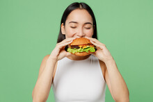 Young Happy Hungry Fun Cheerful Woman Wear White Clothes Holding Eating Biting Tasty Burger Isolated On Plain Pastel Light Green Background Proper Nutrition Healthy Fast Food Unhealthy Choice Concept