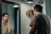 Man Applying Under Eye Patches In Front Of Mirror