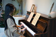 Asian girl playing piano at home, hobbies to enhance concentration and relaxation.