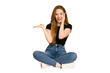 © Asier - Young redhead woman sitting on the floor cut out isolated holds copy space on a palm, keep hand over cheek. Amazed and delighted.