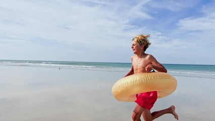 Wall Mural - Handsome boy with inflatable doughnut buoy run on the sea beach