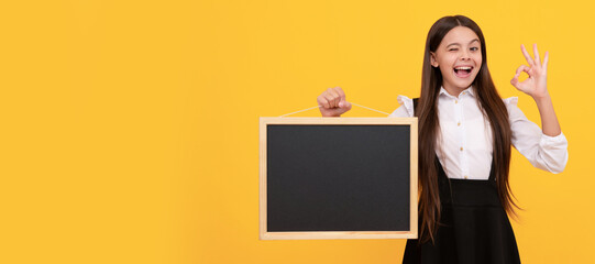 Canvas Print - surprised child in uniform hold school blackboard for copy space showing ok gesture, advertising. Banner of schoolgirl student. School child pupil portrait with copy space.