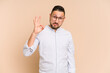 © Asier - Adult latin man cut out isolated winks an eye and holds an okay gesture with hand.
