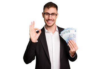 Young business caucasian man holding euro banknotes isolated cut out cheerful and confident showing ok gesture.