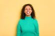 Young Brazilian curly hair cute woman isolated on yellow background funny and friendly sticking out tongue.