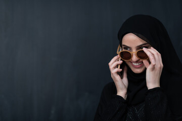 Wall Mural - Young modern muslim business woman using smartphone wearing hijab clothes in front of black chalkboard