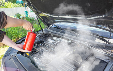 The driver of the car directs a powder fire extinguisher at the engine compartment of the car in which there is fire and smoke. Car fire, background. Electrical short circuit