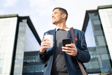 Poster - Businessman at office building with phone, coffee and bag, happy waiting for online taxi service after work. City, business and success, man with smile and 5g smartphone standing outside workplace.