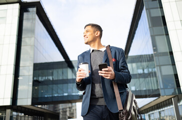 Poster - Businessman outside building with phone, coffee and bag, happy waiting for online taxi service after work. Office, business and success, man with smile holding 5g smartphone standing on city street.