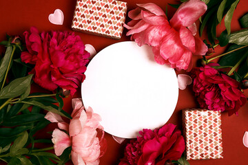 Wall Mural - Festive frame with round blank card, peonies and gifts  on a red background.