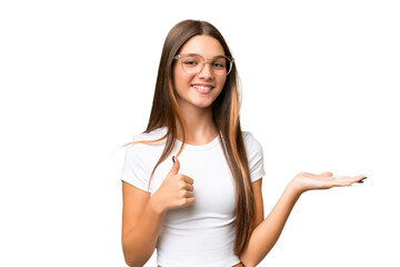 Sticker - Teenager caucasian girl over isolated background holding copyspace imaginary on the palm to insert an ad and with thumbs up