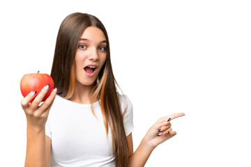 Canvas Print - Teenager caucasian girl holding an apple over isolated background surprised and pointing finger to the side