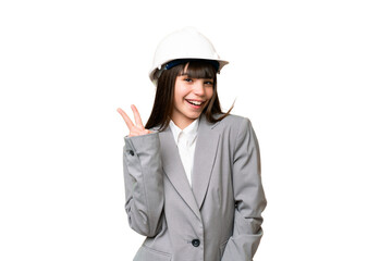 Little girl playing as a architect with helmet and holding blueprints over isolated background smiling and showing victory sign