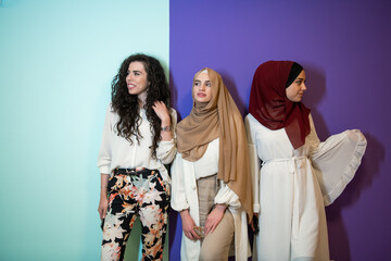 Wall Mural - Group portrait of beautiful muslim women two of them in fashionable dress with hijab isolated on colorful background representing modern islam fashion and ramadan kareem concept