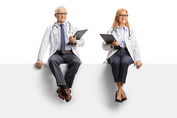 Wall Mural - Male and female doctors sitting on a blank panel and smiling