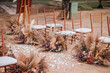 Wedding wooden chairs decorated with flowers. Rustic aisle chairs standing on sand for ceremony on the beach. Natural, shabby, boho wedding decor