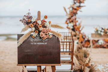 A welcome board sign with a beautiful flower rustic decoration, standing in front of wedding entrance on the beach