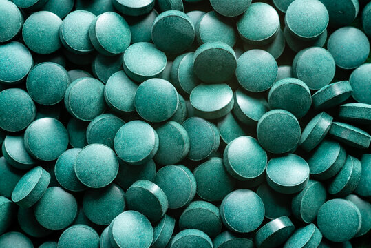 green organic spirulina in algae pills tablets bamboo wood spoon rich in iron close-up super food co