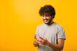 © Vadim Pastuh - Portrait of cheerful Indian man in casual t-shirt using cellphone and smiling, reading good news message, enjoying mobile application. Curly guy with smartphone in hands
