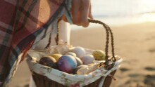 A Woman Carries A Wicker Basket With Easter Eggs, The Setting Sun And The Wind Blows The Plaid On It. Sea Sand And Waves In The Background. Slow Motion.
