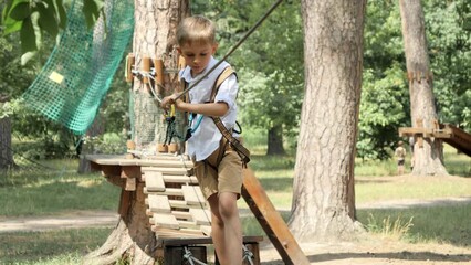 Wall Mural - Little boy struggling walking on strung rope between trees in park. Active childhood, healthy lifestyle, kids playing outdoors, children in nature