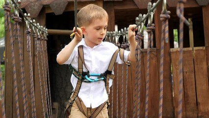 Canvas Print - Portrait of brave boy crossing bridge made of planks and ropes at extreme adventure park. Kids sports, summer holiday, fun outdoors, scouts