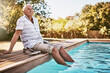 Relax, retirement and thinking with old man by swimming pool and for summer, peace and happy. Smile, calm and vacation with senior citizen with feet in water on break for happiness, holiday and fun