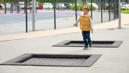 Wall Mural - Little boy running on public playground and jumping over trampolines. Active child, sports and development, kids playing outdoors.