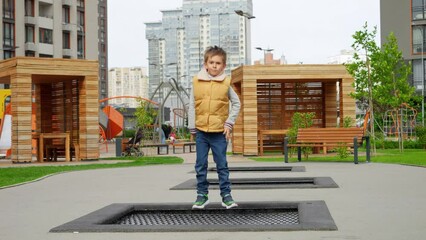 Wall Mural - Slow motion of little boy pretending flying as he jumps on trampoline at new public playground. Active child, sports and development, kids playing outdoors.