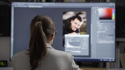 Back view of female professional photographer works in photo editing app software on full screen computer. Freelance photo editor retouching photos.Image editing software mock-up. 4k footage