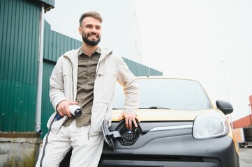 man holding power charging cable for electric car in outdoor car park. and he s going to connect the