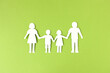Familie mit Mutter, Vater und zwei Kindern, die sich an den Händen hält, als Silhouette aus weißem Papier ausgeschnitten auf grünem Hintergrund
