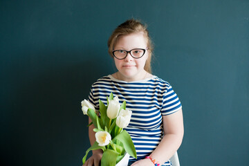 Wall Mural - Portrait of teenage girl with Down syndrome standing with flowers on blue background. Disability children. World Down syndrome day.