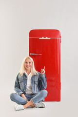 Sticker - Mature blonde woman pointing at retro fridge on light background