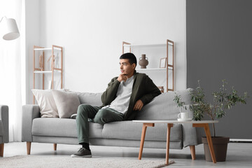 Wall Mural - Thoughtful young man sitting on sofa at home