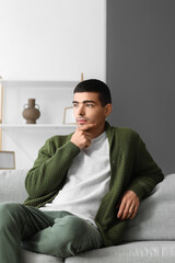 Poster - Thoughtful young man sitting on sofa at home