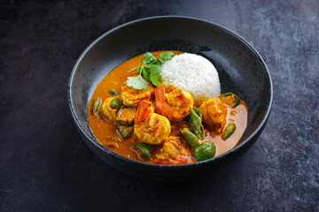 Wall Mural - Traditional Thai kaeng phet red curry prawn with chili and basmati rice served as close-up in a Nordic design bowl