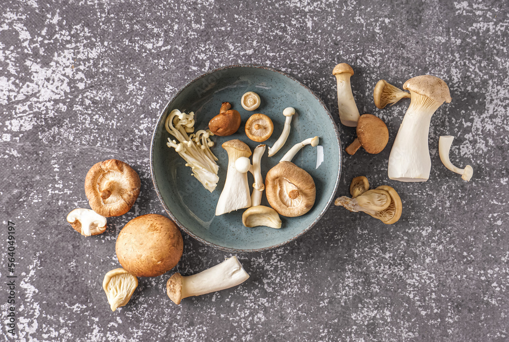 Bowl with different fresh mushrooms on grunge background