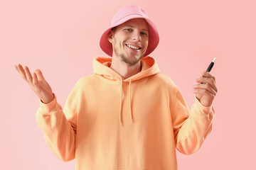 Wall Mural - Young man in bucket hat with disposable electronic cigarette on pink background