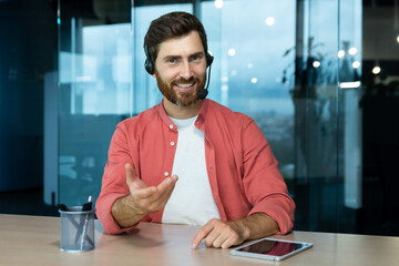 Wall Mural - Webcam pov view, man in office with headset for video call smiling and looking into camera, businessman seller online communicates with customers, works remotely laptop at online meeting colleagues