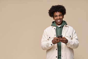 Smiling cool ethnic guy holding smartphone isolated on light beige background. Happy African American teenager using mobile cell phone advertising shopping or social network apps commercial promotion.