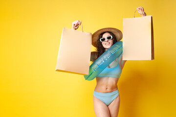 Wall Mural - young attractive brunette girl in a blue swimsuit with a swimming inflatable ring holds packages with purchases