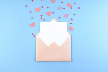 pink envelope with blank white paper card inside and valentine hearts on pastel blue background. rom