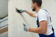 © New Africa - Professional worker plastering wall with putty knives indoors