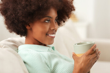 Wall Mural - Smiling African American woman with cup of drink at home